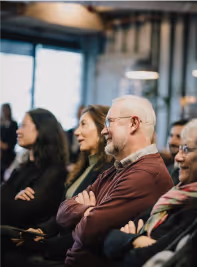 Group of diverse adults attentively listening and seated in an indoor setting.
