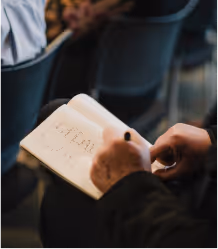 Person writing in a notebook with a pen, focused on handwritten text on the page.