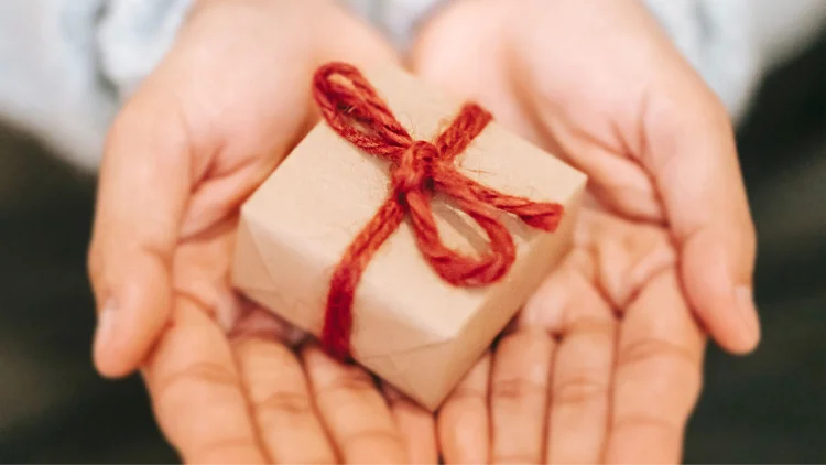 Hands hold a tiny package wrapped with red string