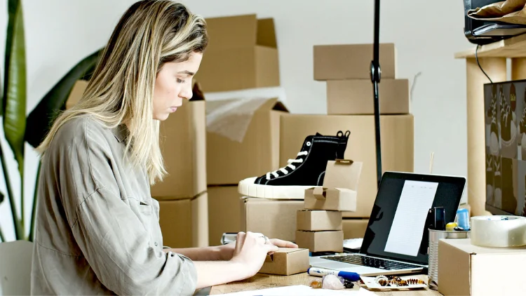 Woman sits with laptop and packs boxes with shoes