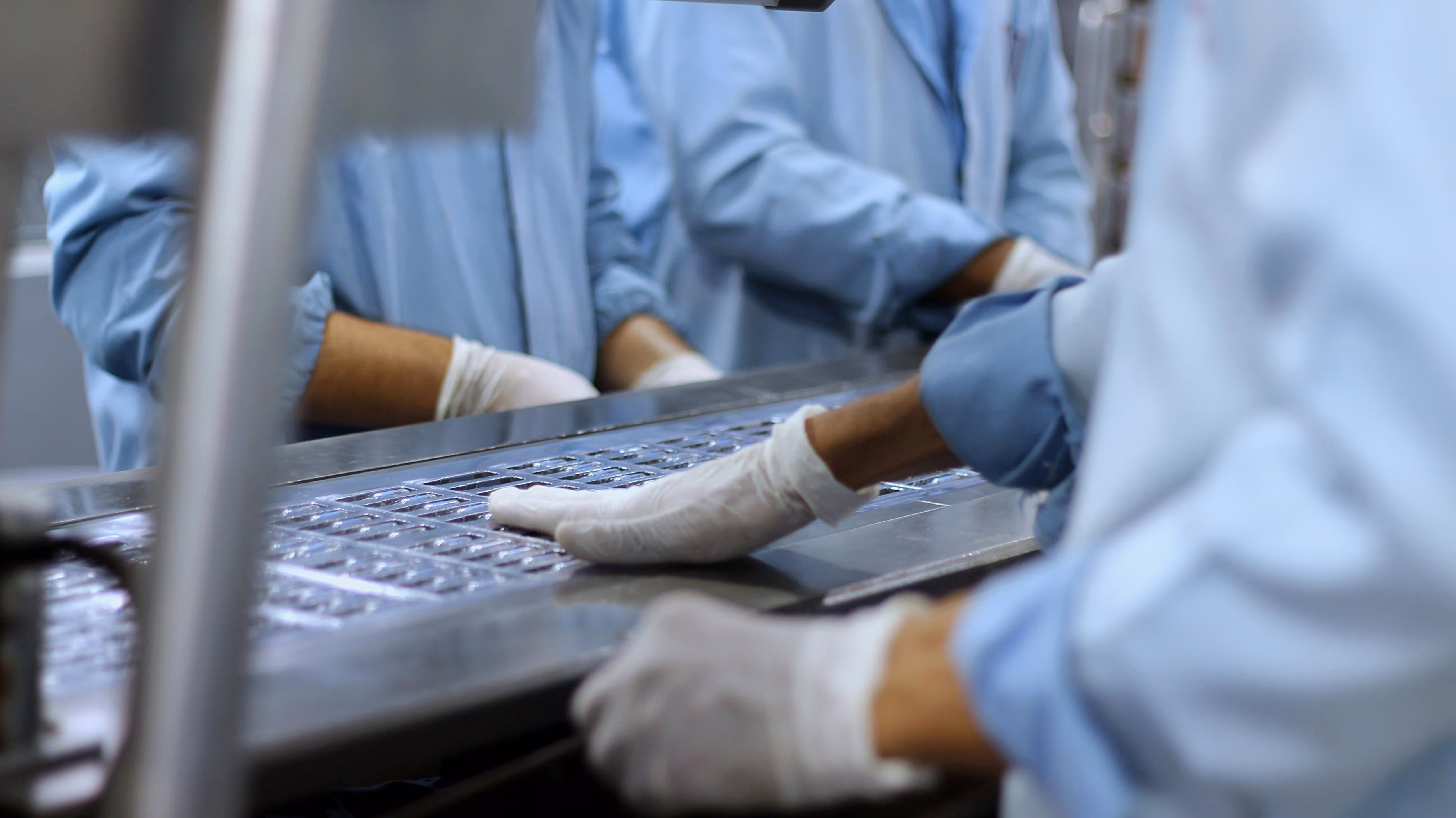 Workers in blue uniforms and gloves handling a metal tray with multiple small compartments.