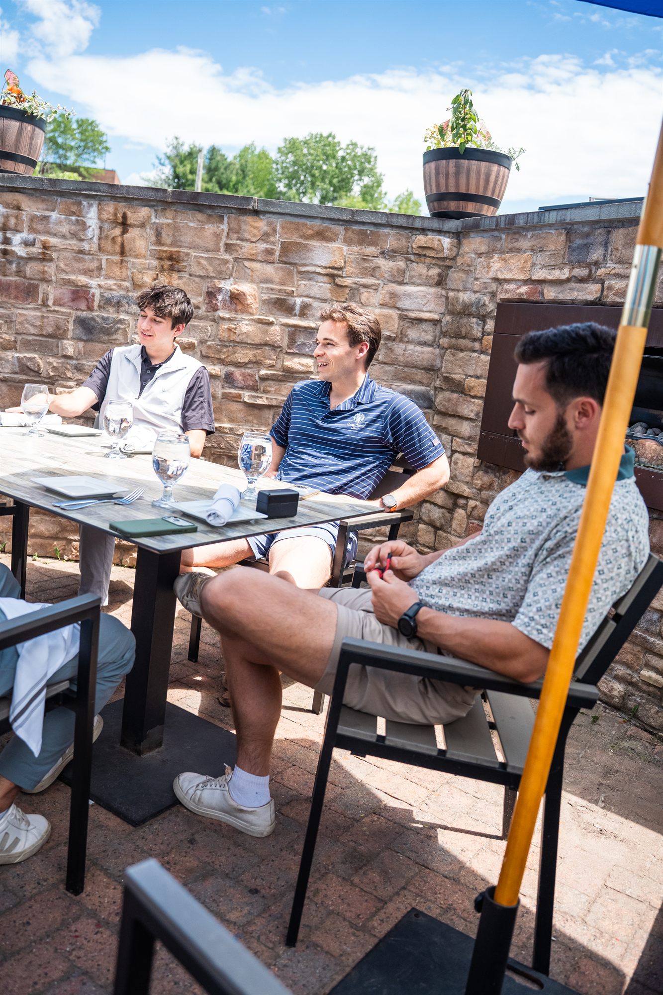 Three teammates relaxing at a sunny stone-walled patio table over lunch