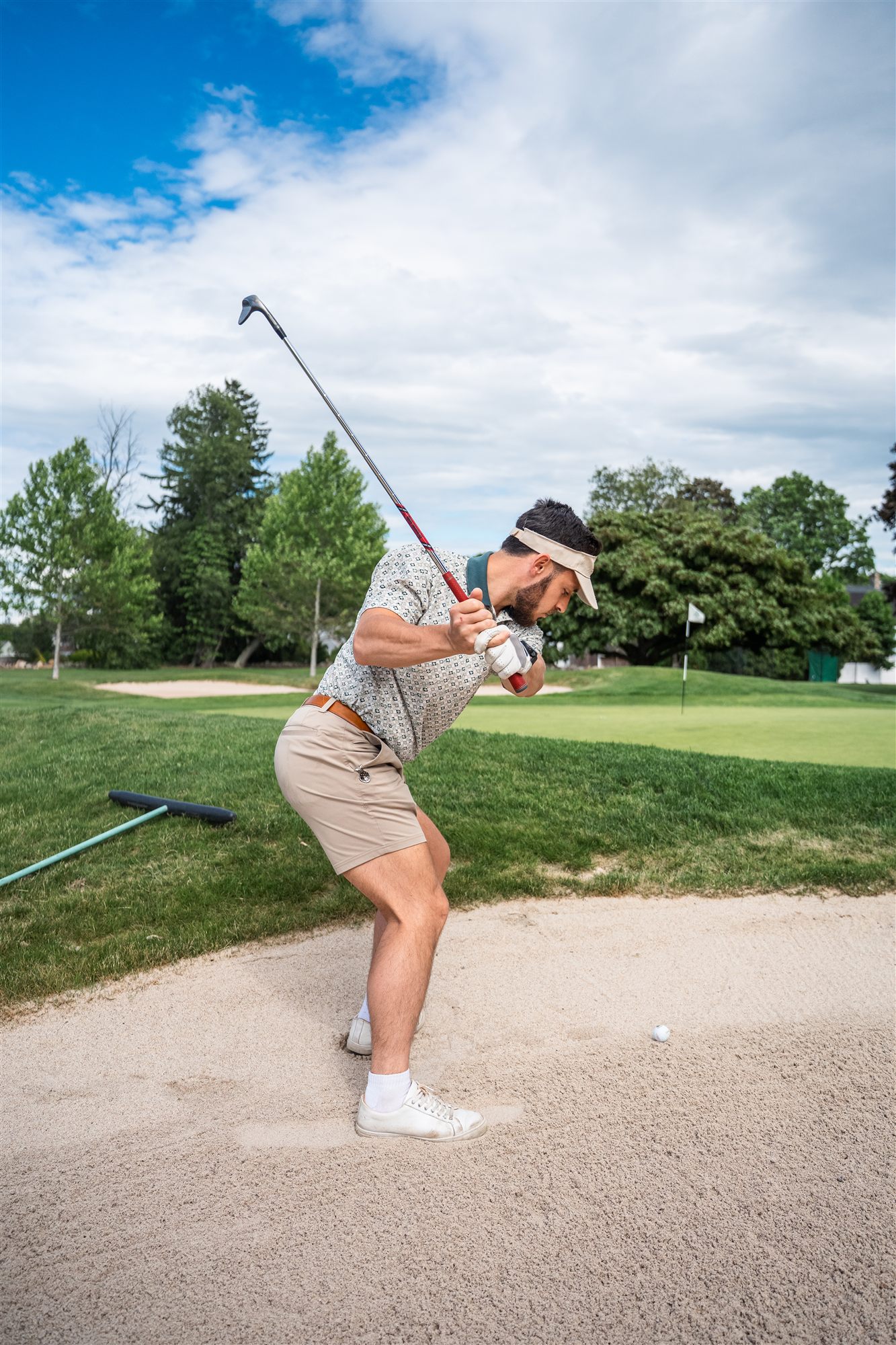 Golfer at full backswing in the bunker under a dramatic blue sky