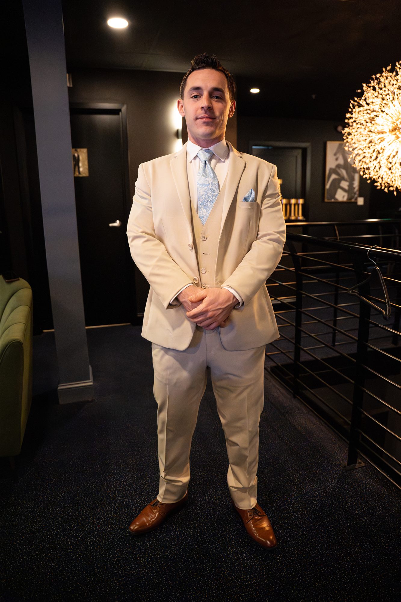 Smiling guest in a cream three-piece suit beside a chandelier in the lounge
