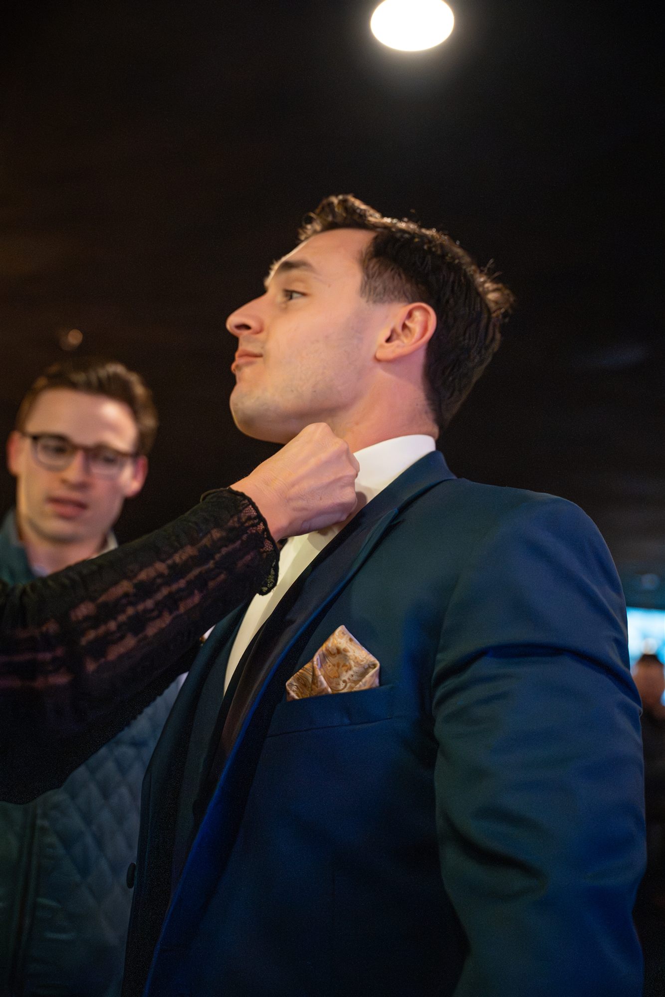 Woman adjusting a man's tuxedo collar backstage before the runway