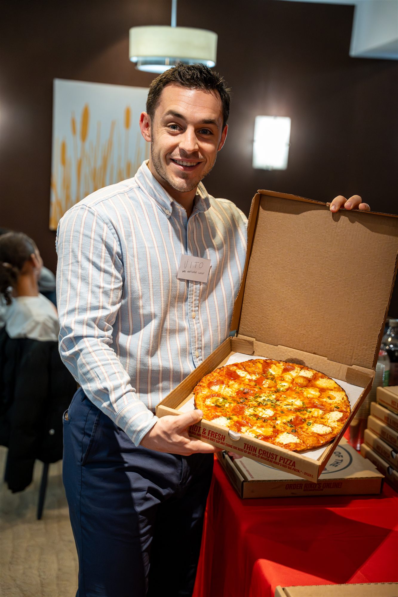 Beaming AFC team member presenting an open box of fresh pizza