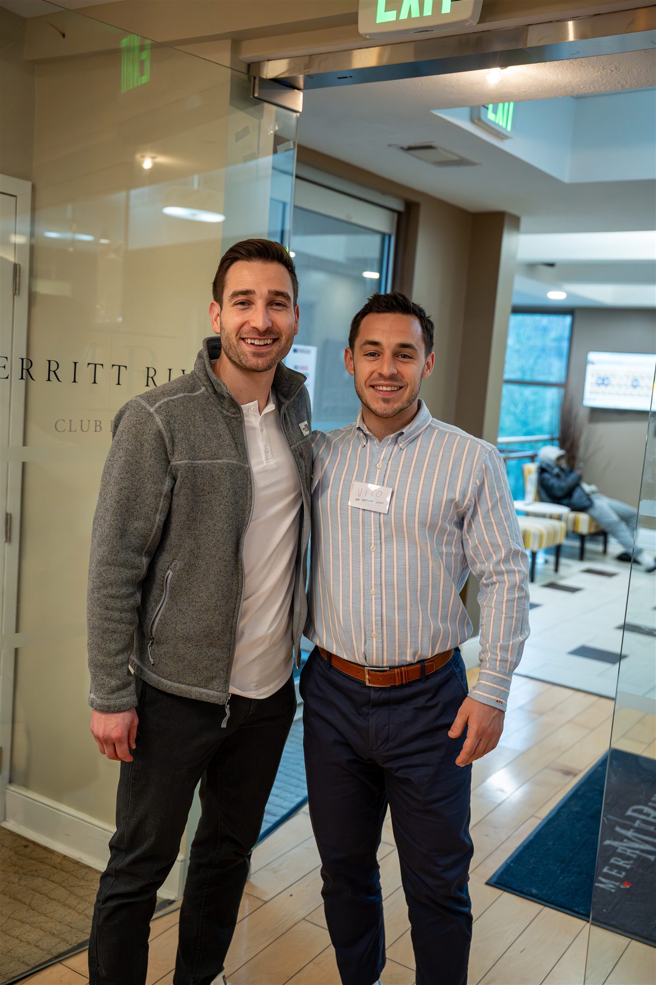 Two smiling AFC team members at the glass entrance of the club room