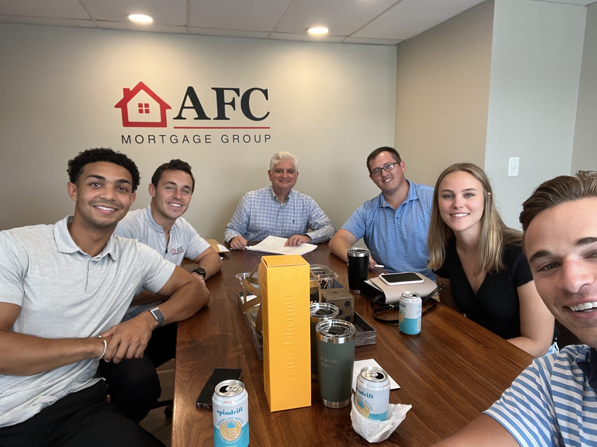Justin and Sarah celebrating closing day with drinks and a gift box in the AFC office