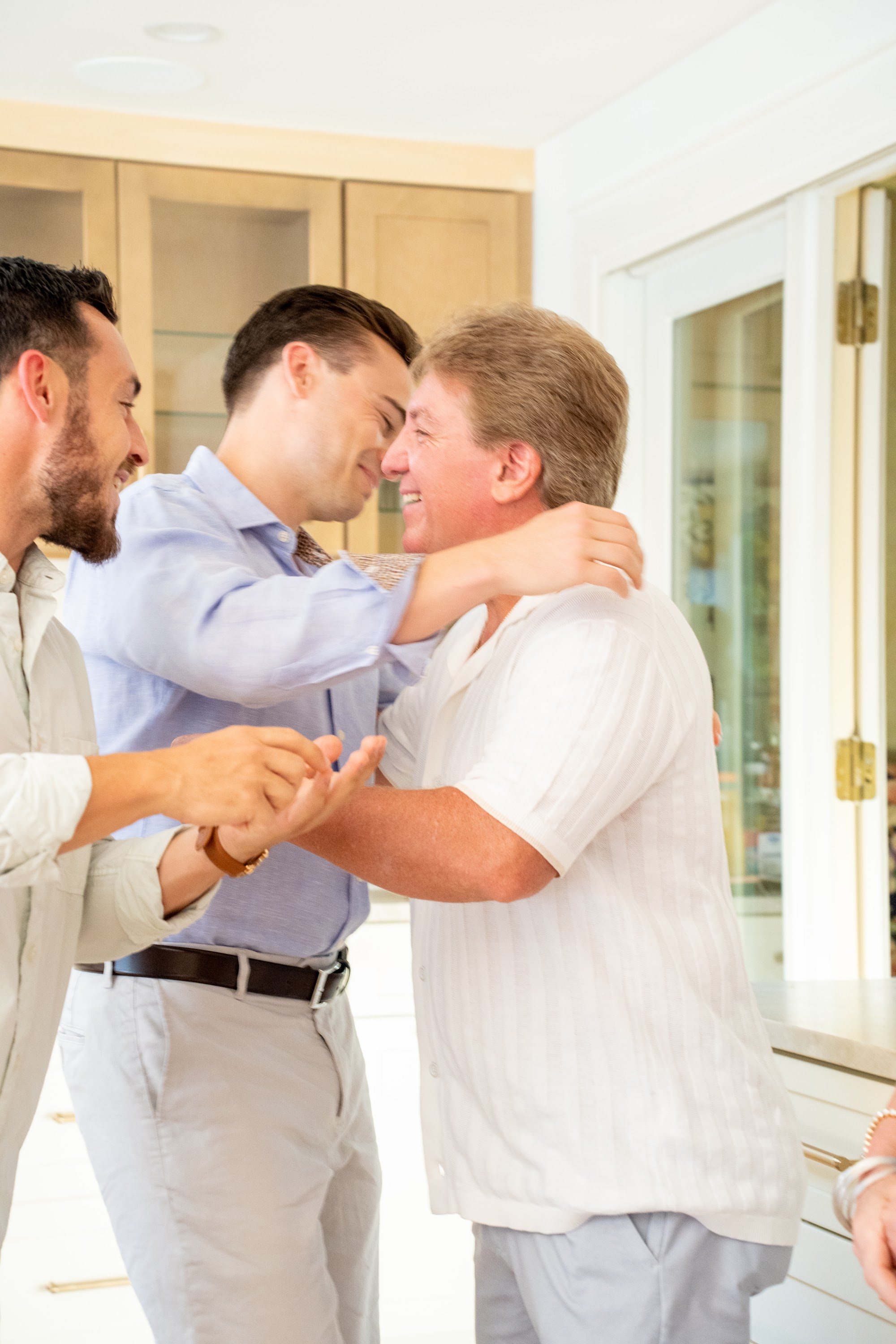 Three guests laughing and hugging in the kitchen at the investor dinner