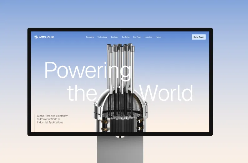Computer monitor displaying the ZettaJoule homepage with a metallic industrial device centered against a blue to cream gradient background, featuring the text 'Powering the World' and a tagline about clean heat and electricity for industrial applications.