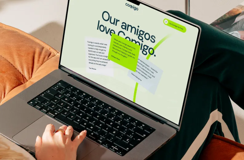 Person using a laptop showing a webpage with the heading 'Our amigos love Comigo' and customer testimonials in colored boxes on the screen.