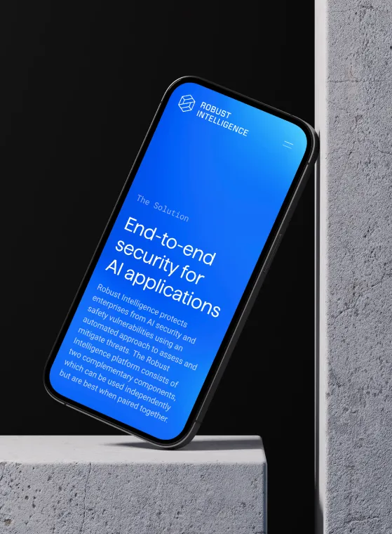 Smartphone with a blue screen leaning on a gray concrete surface displays Robust Intelligence branding and text about end-to-end security for AI applications, describing protection of enterprises from AI security and safety vulnerabilities using an automated approach.