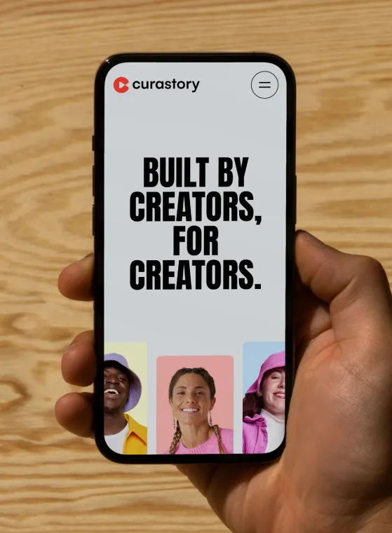 A hand holding a smartphone displaying the Curastory logo and the text 'Built by creators, for creators.' The bottom of the screen shows three small portraits of diverse smiling individuals with colorful backgrounds.