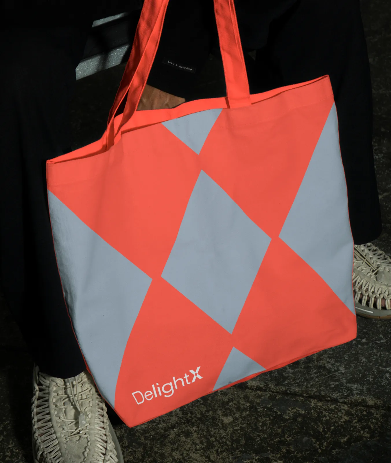 Orange and gray patterned tote bag with the word DelightX held by a person wearing black pants.