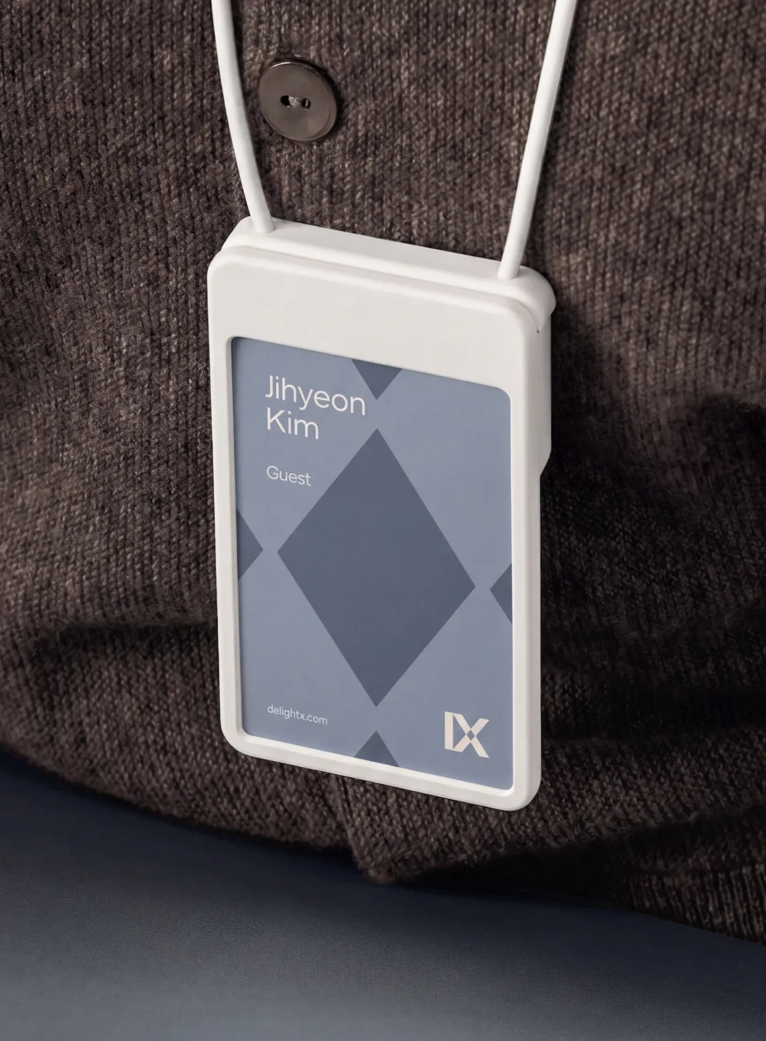 Close-up of a visitor badge worn on a dark brown knitted sweater, showing the name Jihyeon Kim, the label Guest, and a blue design with the DelightX logo and website.