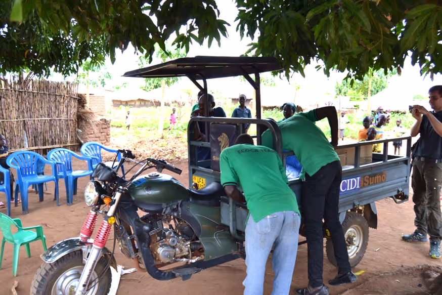 Refugee settlement, Uganda. 
 In the picture: technical advisors & assembly staff, modified motorcycle for delivery