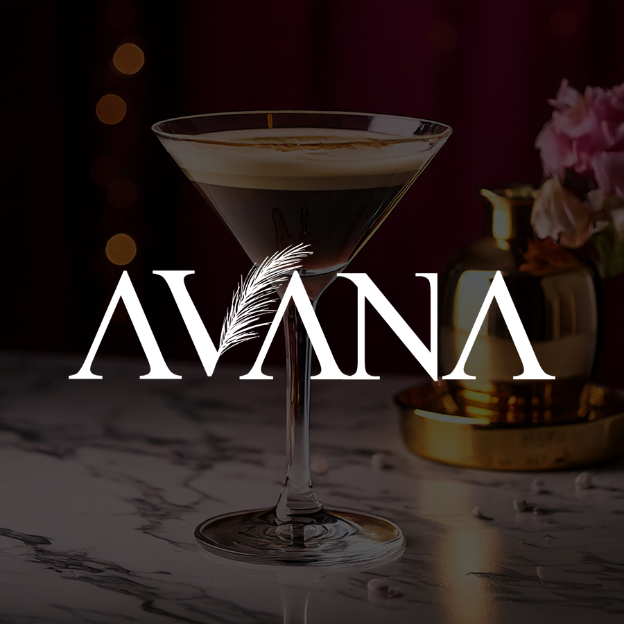 Espresso martini cocktail in a glass on a marble surface with a blurred background, featuring the text 'AVANA' with a feather integrated into the lettering.