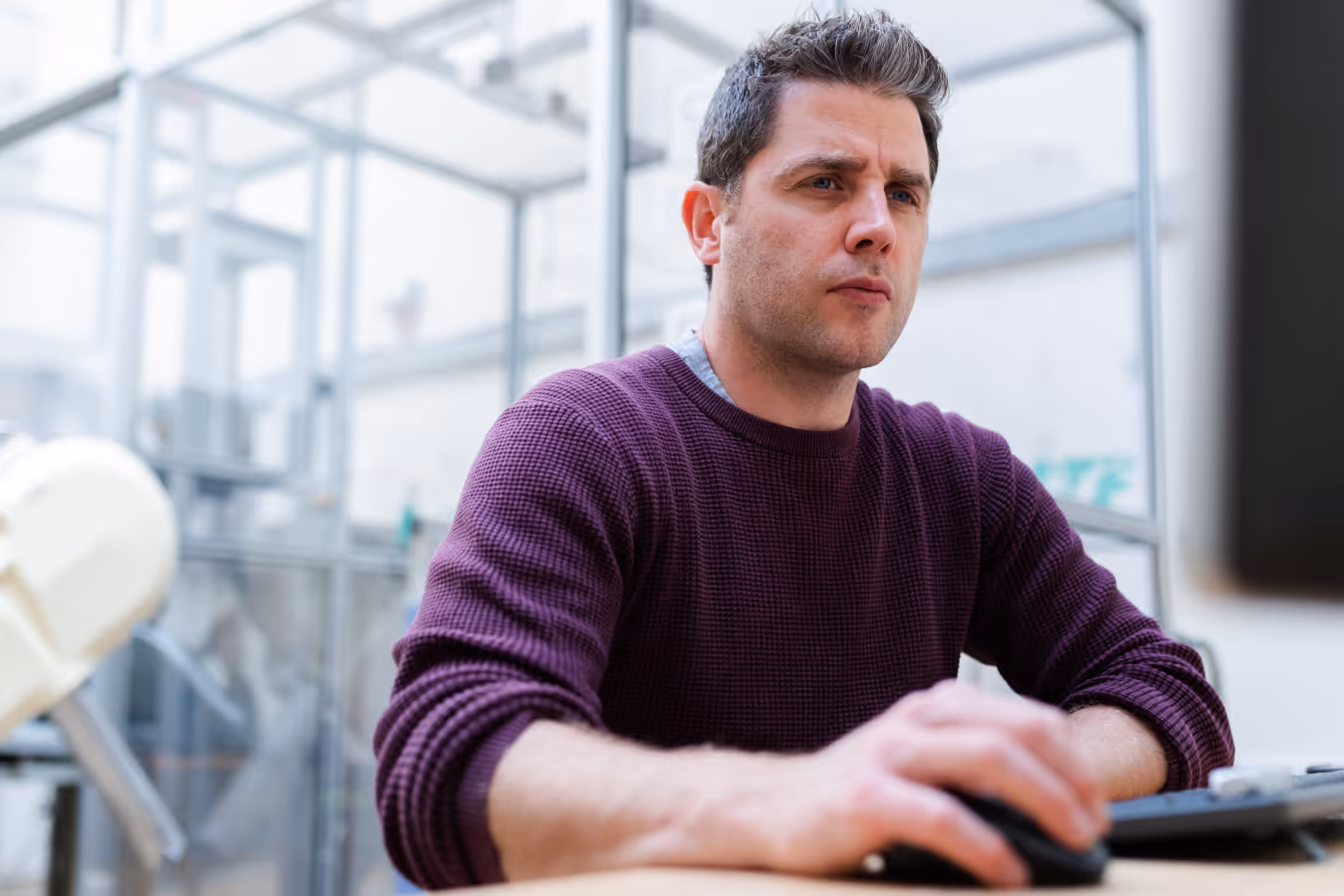 Man in a purple sweater focused on working at a computer in a bright modern office.