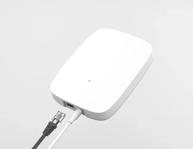White rectangular IoT device with one black Ethernet cable unplugged and one white cable plugged in.