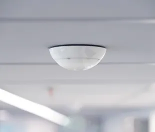 White dome-shaped IoT device detector mounted on a ceiling in a hallway.
