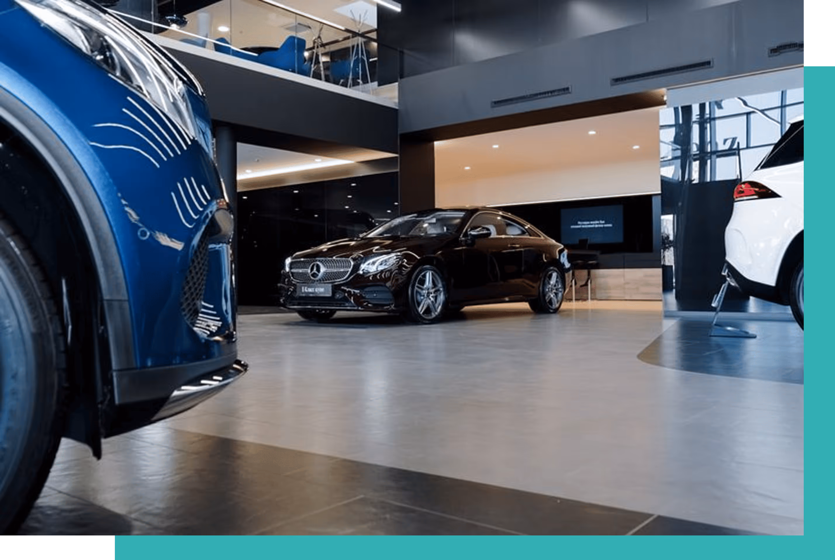 Black Mercedes-Benz coupe displayed in a modern car showroom with a blue car partially visible on the left and a white car on the right.
