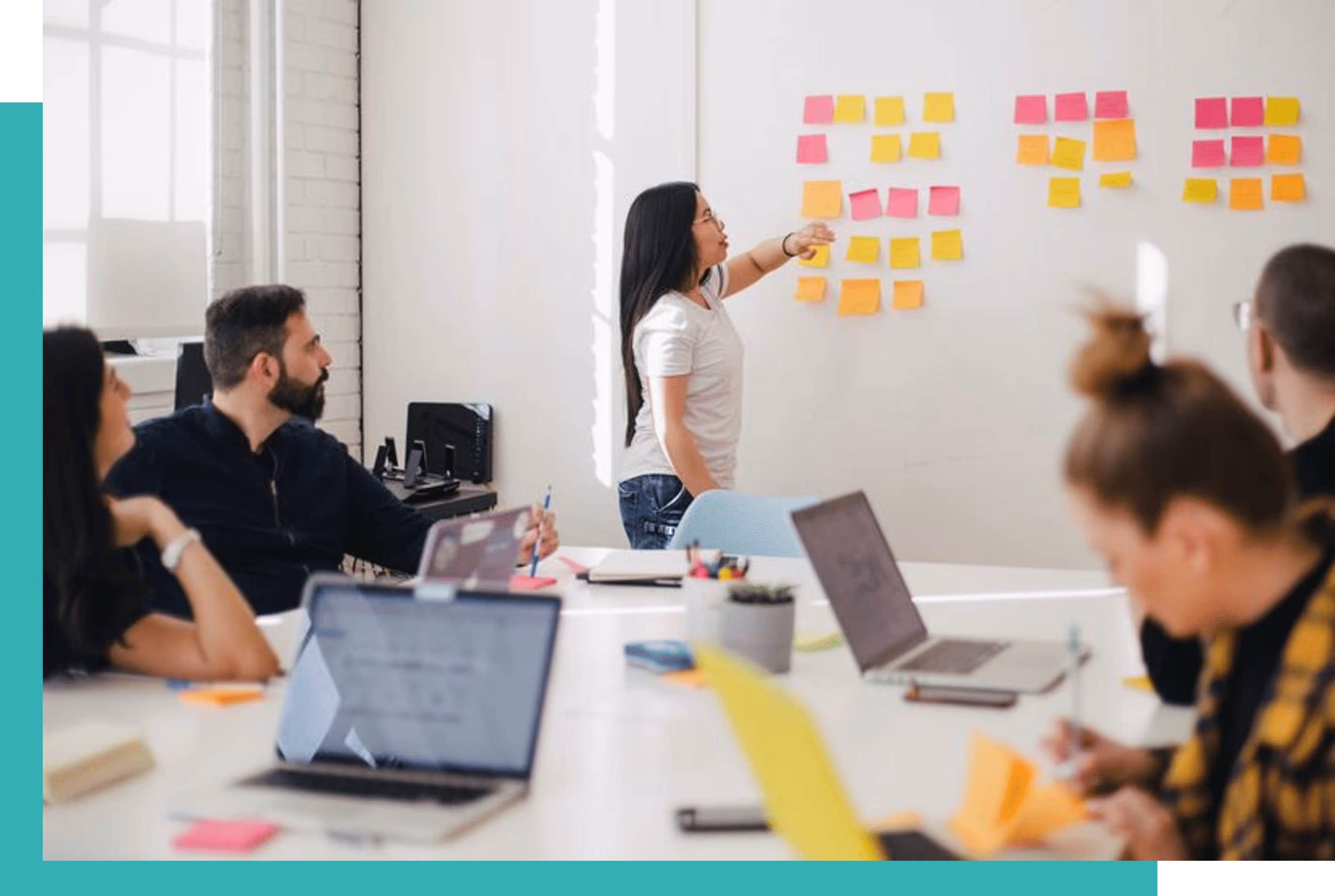A woman presenting ideas on sticky notes to colleagues seated around a white table in a bright office.