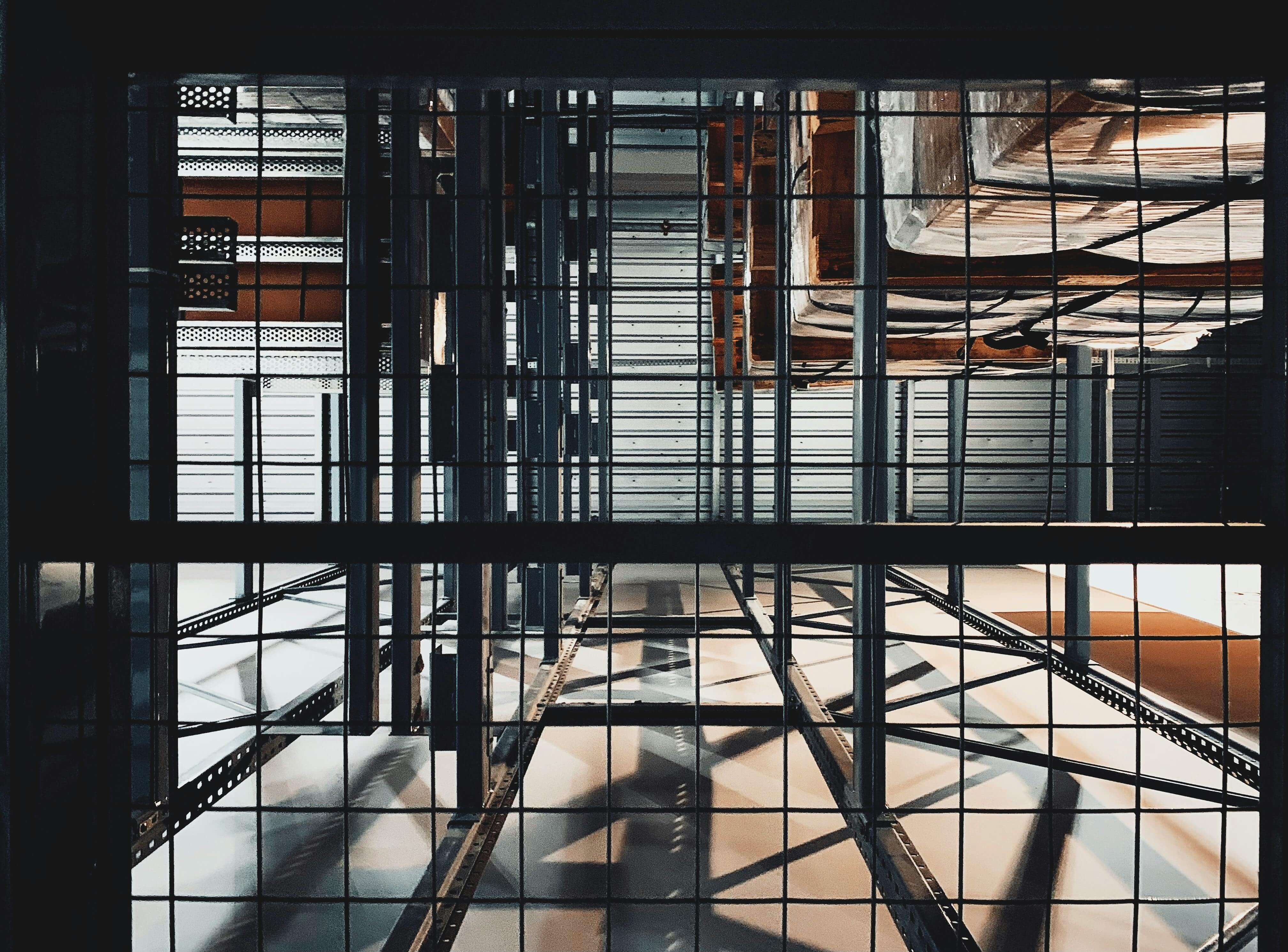 View through a metal grid of industrial shelving with shadows and stacked wooden crates.