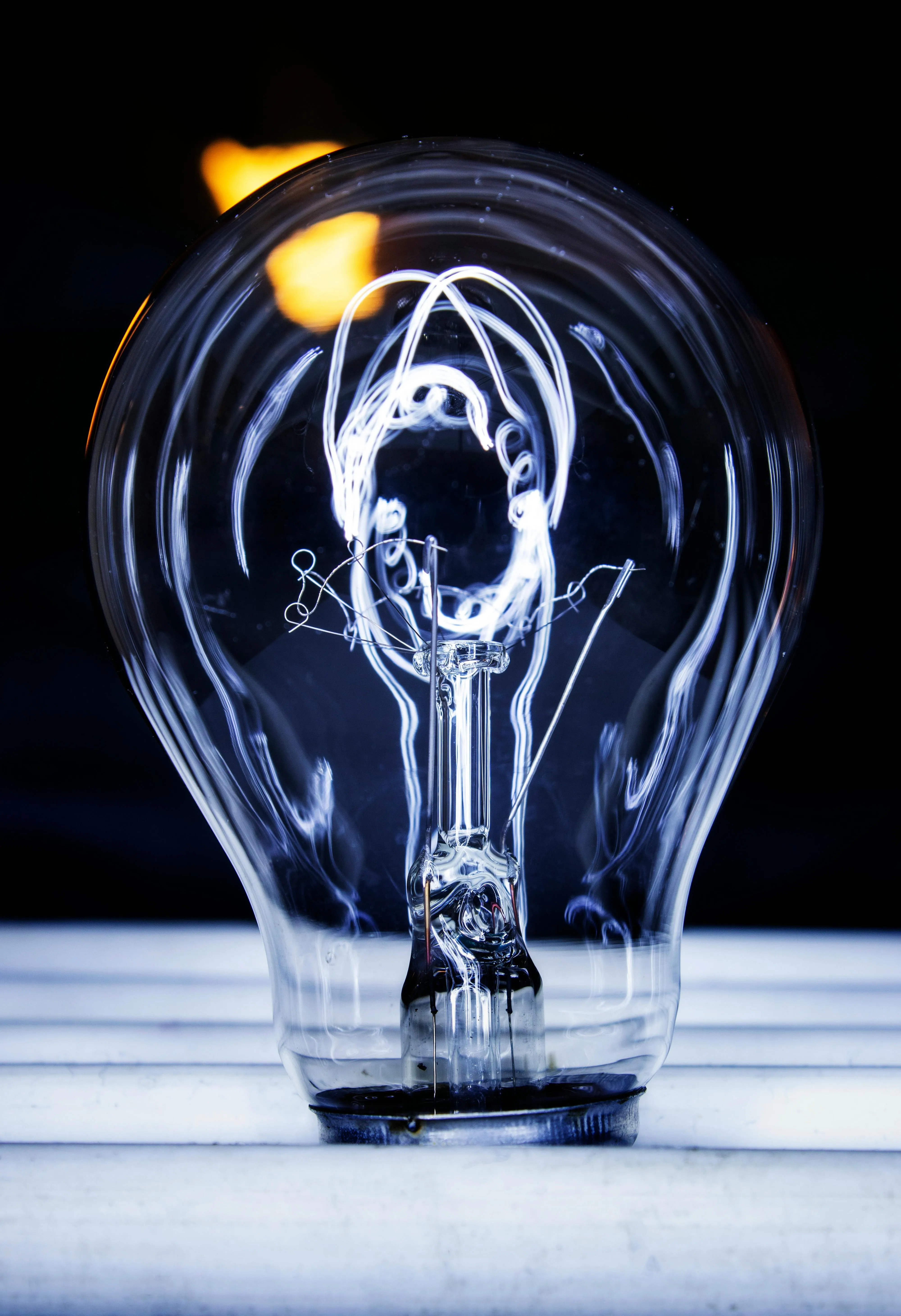 Close-up of a clear light bulb with intricate filament detail against a dark background.