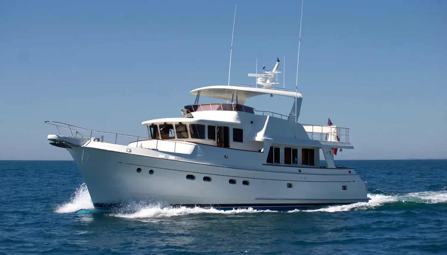 Ocean-going sailing yachts cruising through deep blue waters, showcasing a spacious white exterior with multiple decks and antennas.
