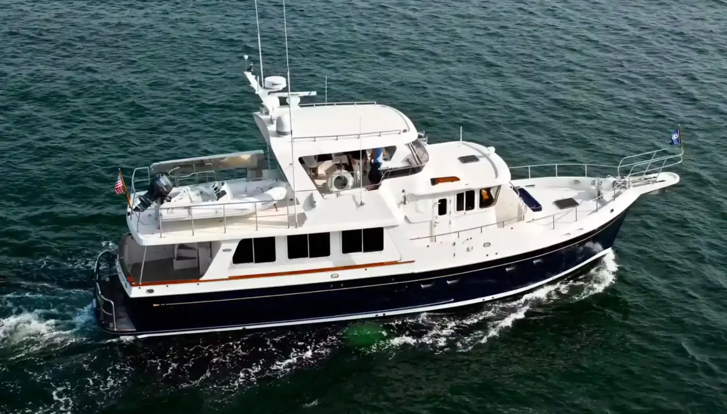 Small ocean-going yachts with a sleek black and white hull, flybridge, and tender boat, navigating calm open waters.