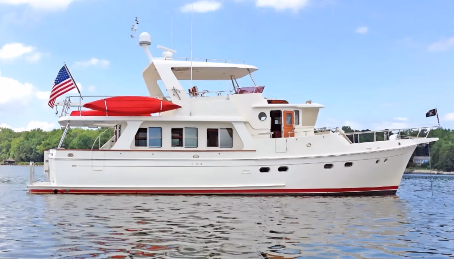 Ocean trawler with elegant white exteriors and red accents, equipped with a flybridge, American flag, and a red kayak on deck