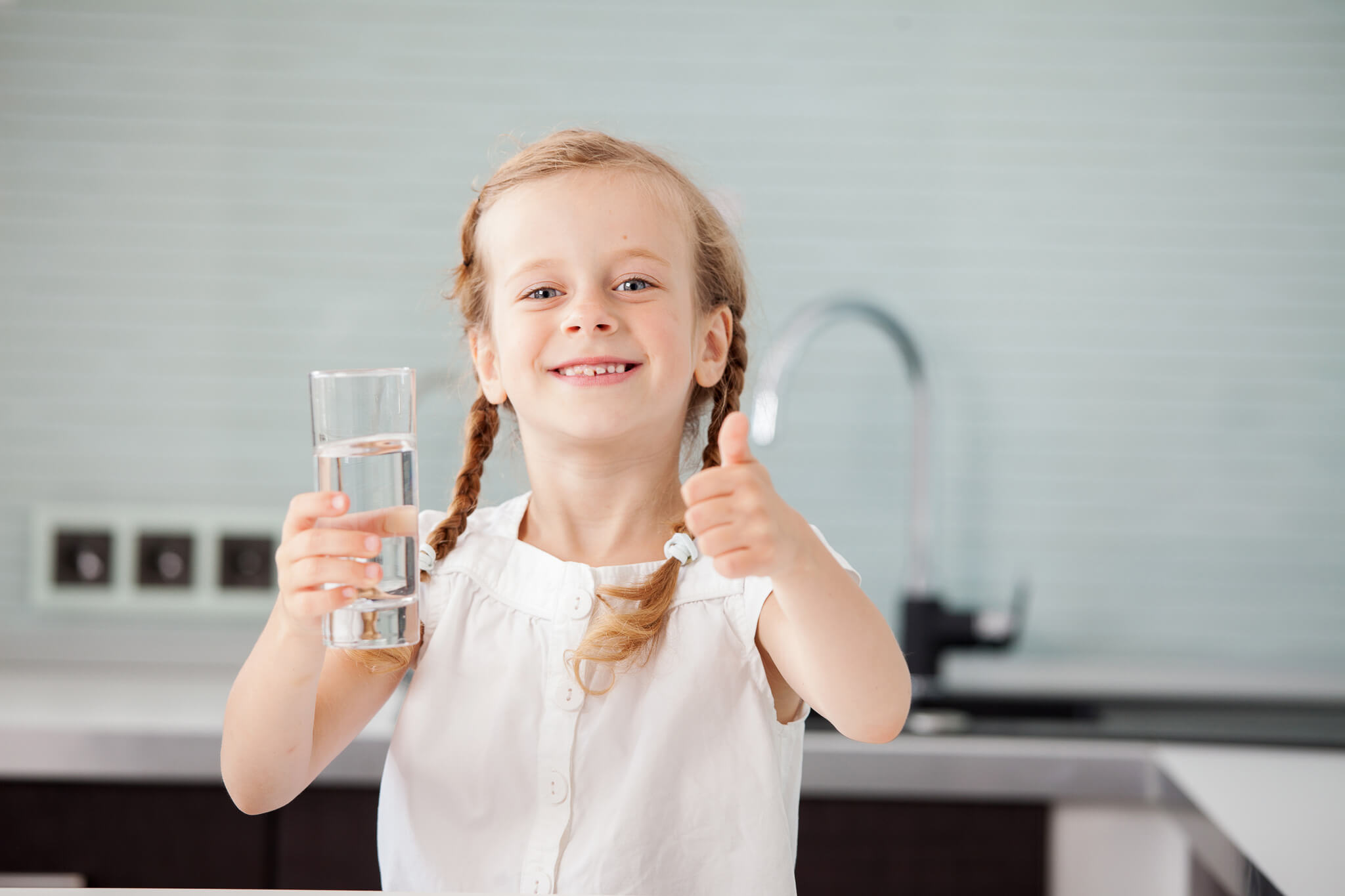 Little girl in white t-shirt with a thumbs up holding a clear glass of water | PerfectWater