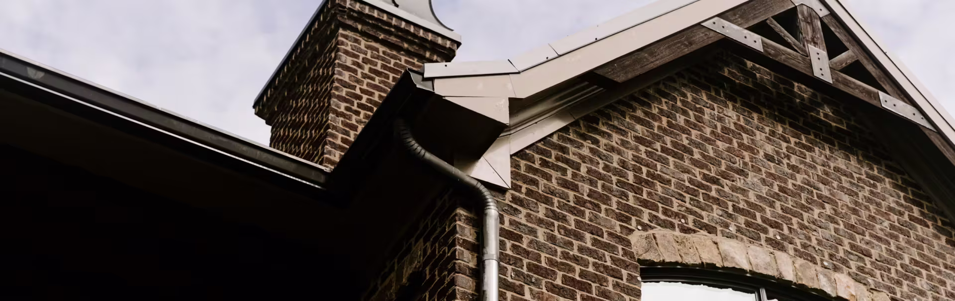 Close-up of a brick house corner showing a chimney, large window, gutter,