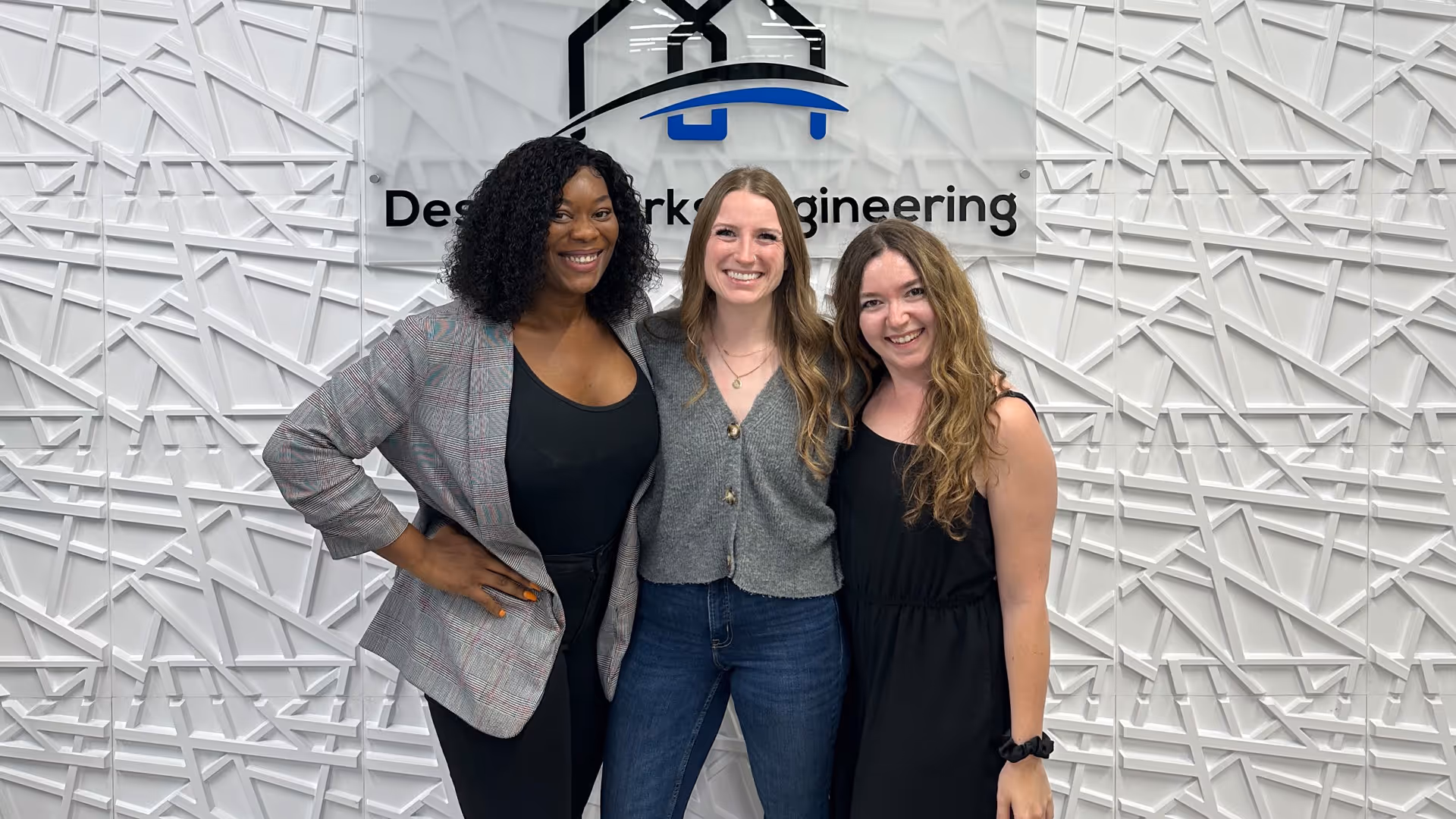 three women standing in front of a wall with a sign that says design engineering