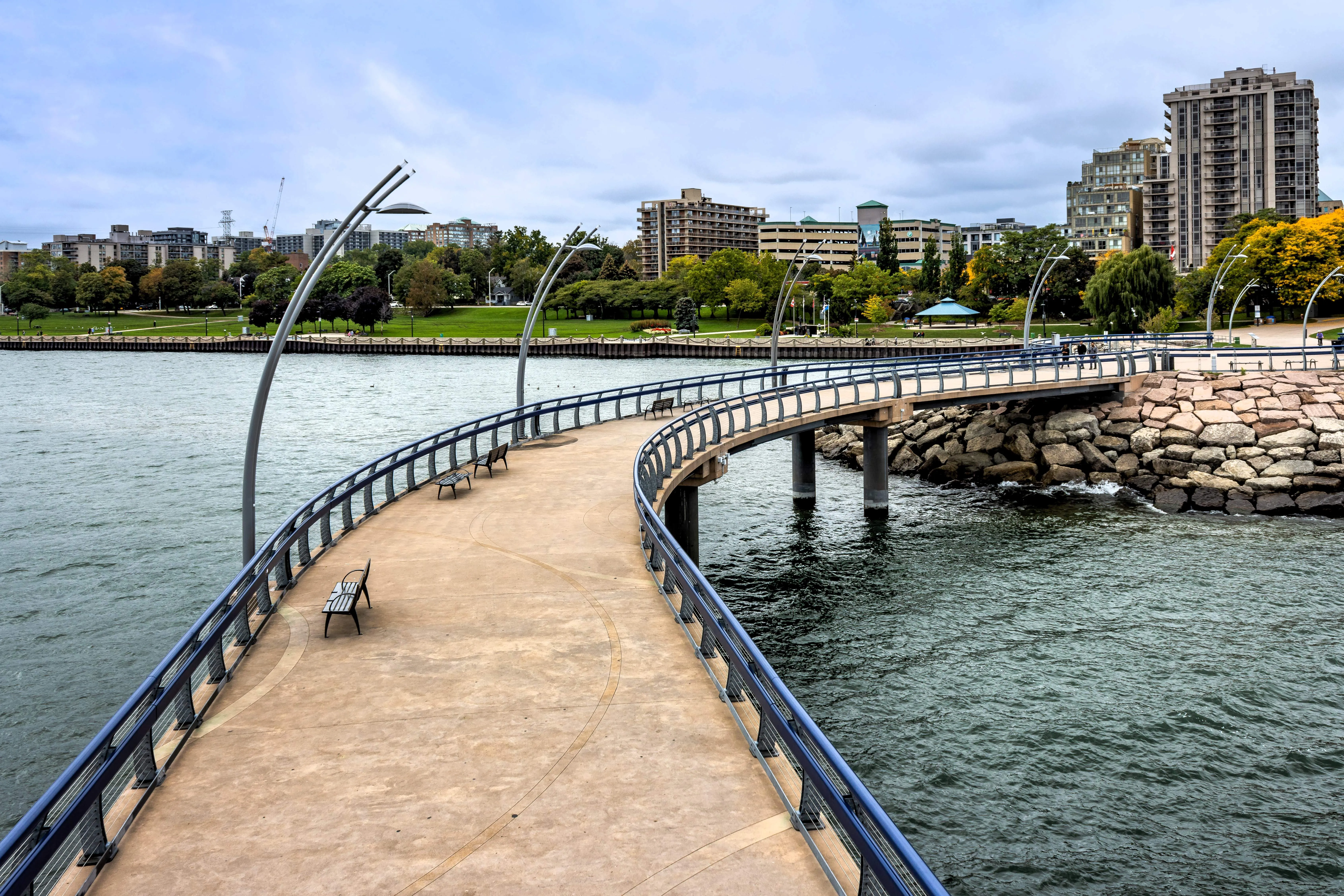 Curved waterfront boardwalk with benches, overlooking urban skyline and lake