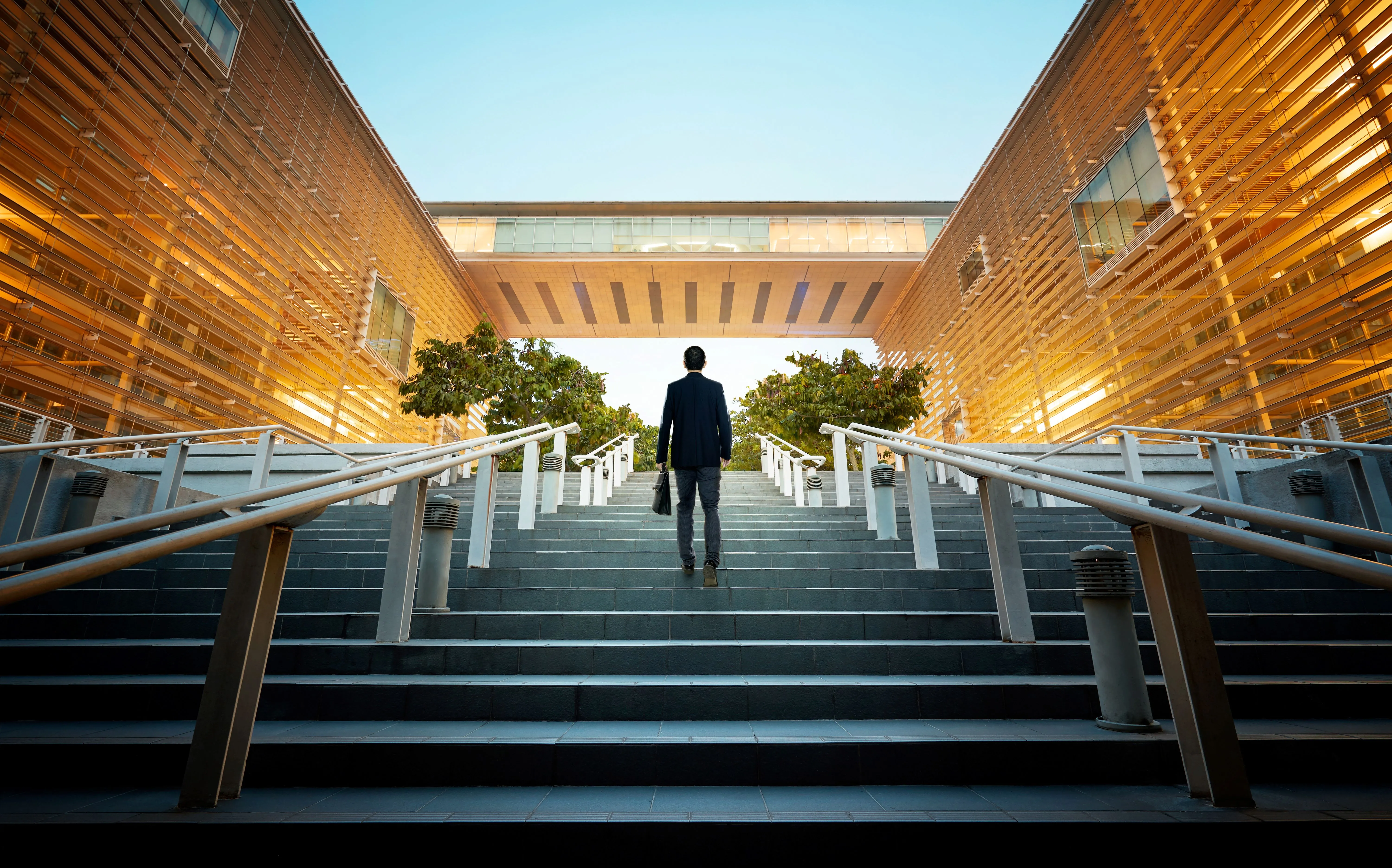 Person climbing stairs between modern golden-toned buildings at sunset