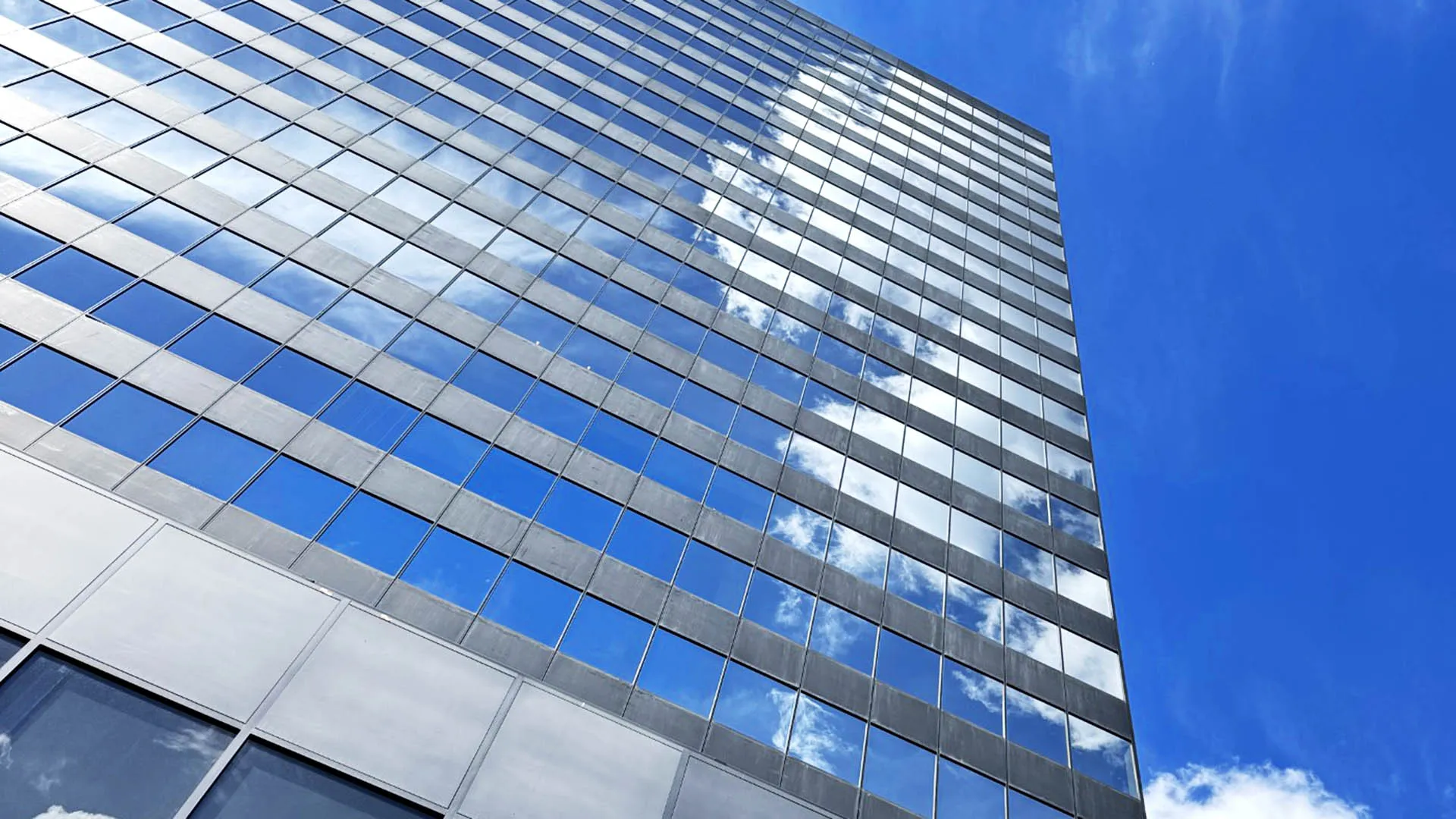 Modern glass skyscraper reflecting blue sky and clouds at an angle
