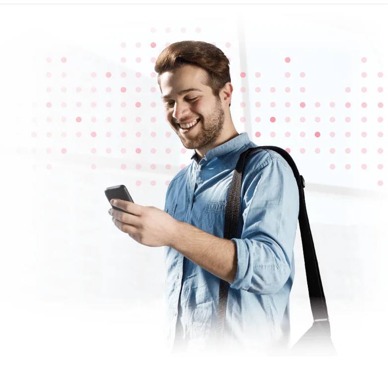 Smiling man in blue shirt looking at smartphone while carrying shoulder bag.