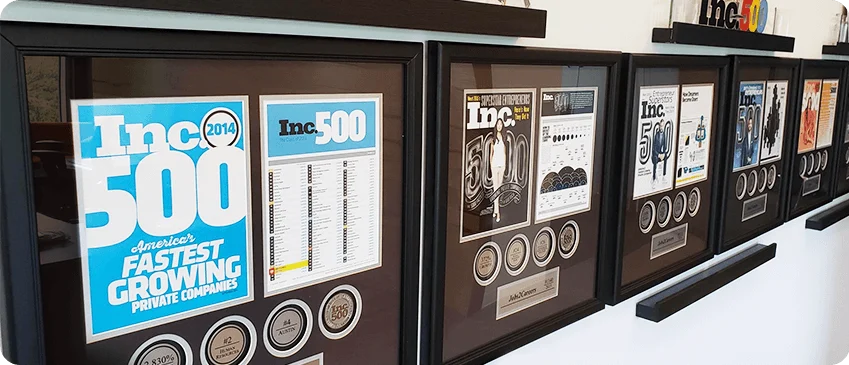 Wall display of framed Inc. 500 awards recognizing fastest growing private companies from multiple years.