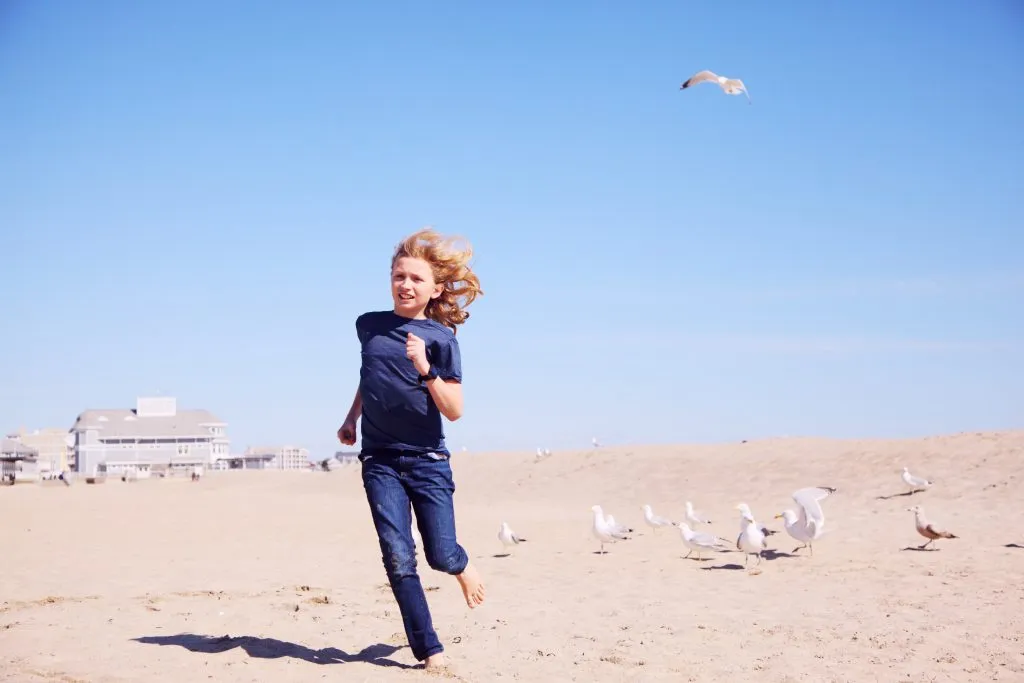 a little girl in blue running on a sandy beach