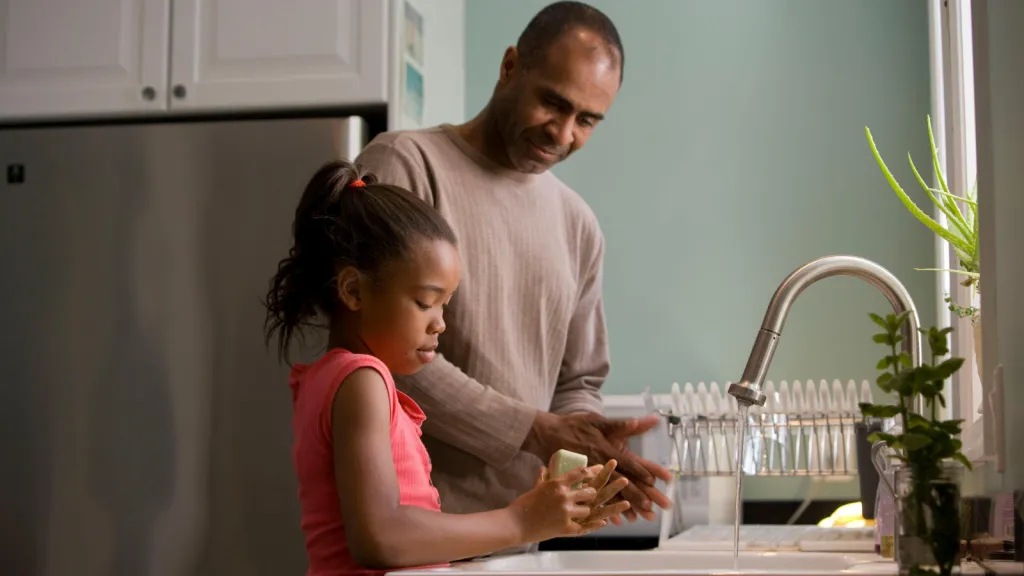 man and girl wash their hands in a kitchen