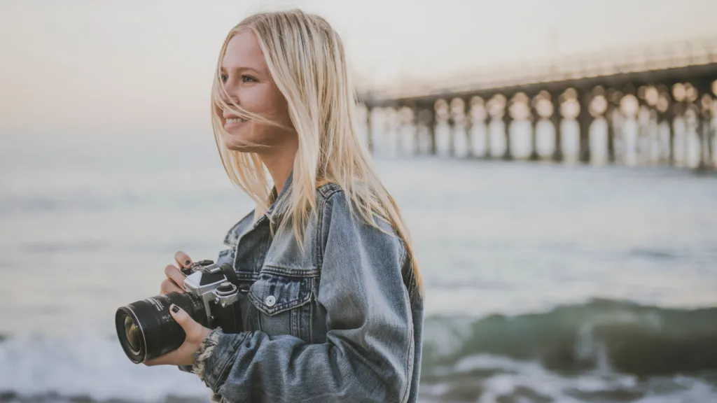 a woman holding a camera standing in front of the ocean