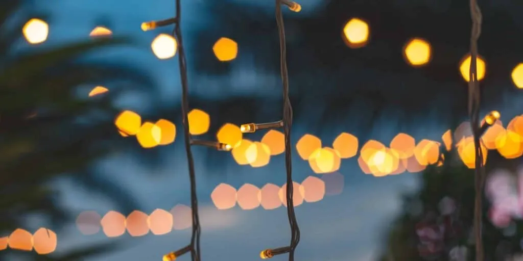 blurred light bokeh with coconut palm tree background on sunset, yellow string lights with bokeh decor in outdoor restaurant.