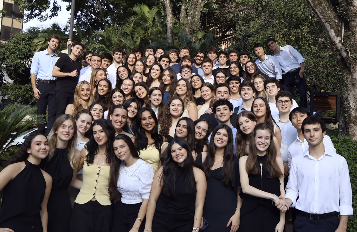 Grupo de jovens adultos, homens e mulheres, posando juntos ao ar livre diante de árvores e plantas.