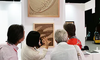 4人の男女が壁に掛かったアート作品を見て説明をしている。