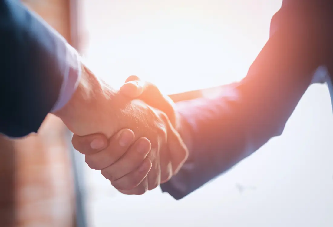 Kaksi ihmistä kättelee, symboloi luottamusta, yhteistyötä ja hyvin hoidettua yrityksen tietoturvaa sekä turvallista taloushallinnon kumppanuutta.