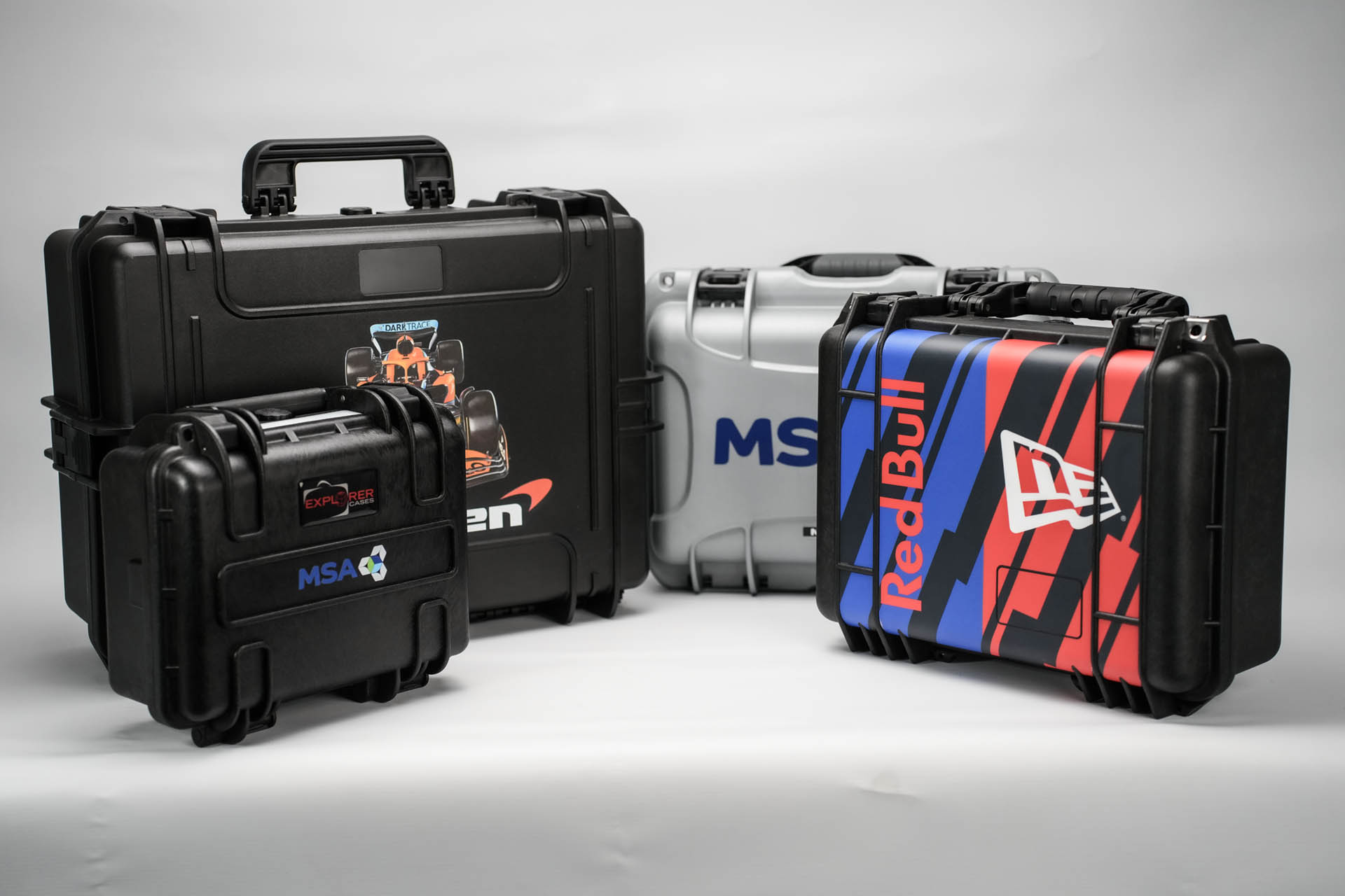 Collection of custom branded protective cases for McLaren, Red Bull, MSA Foams and Explorer, displayed against a studio background