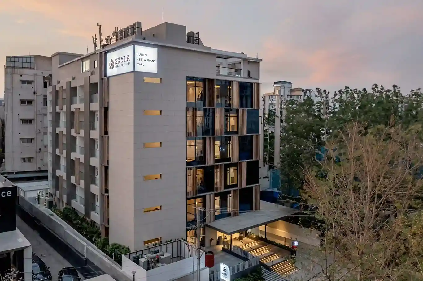 A frontal view of Skyla Studios & Suites located in Hitech City, Madhapur, Hitex, Kondapur, and Road No.45, Jubilee Hills. The well-lit elevation of the hotel building is set in the backdrop of an evening sky in Hyderabad.