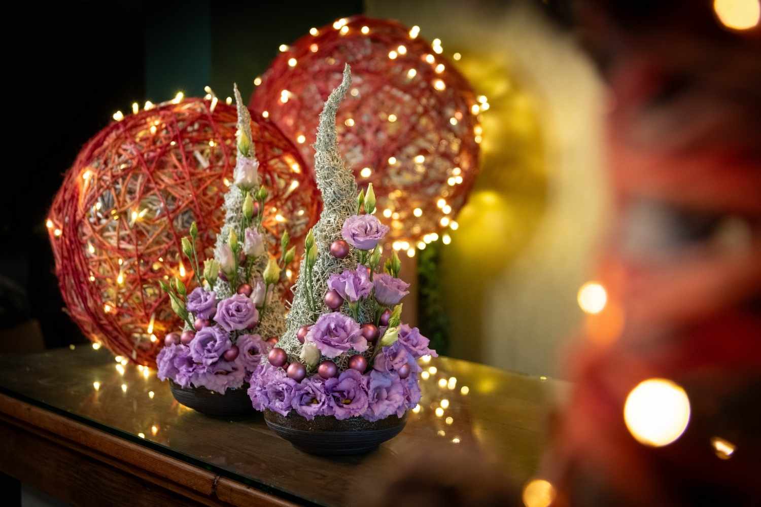 Two conical fresh flower Christmas arrangement designs: vibrant lavender Lisianthus (Eustoma) blooms and buds with moss-wrapped spires as a unique Christmas decor idea.