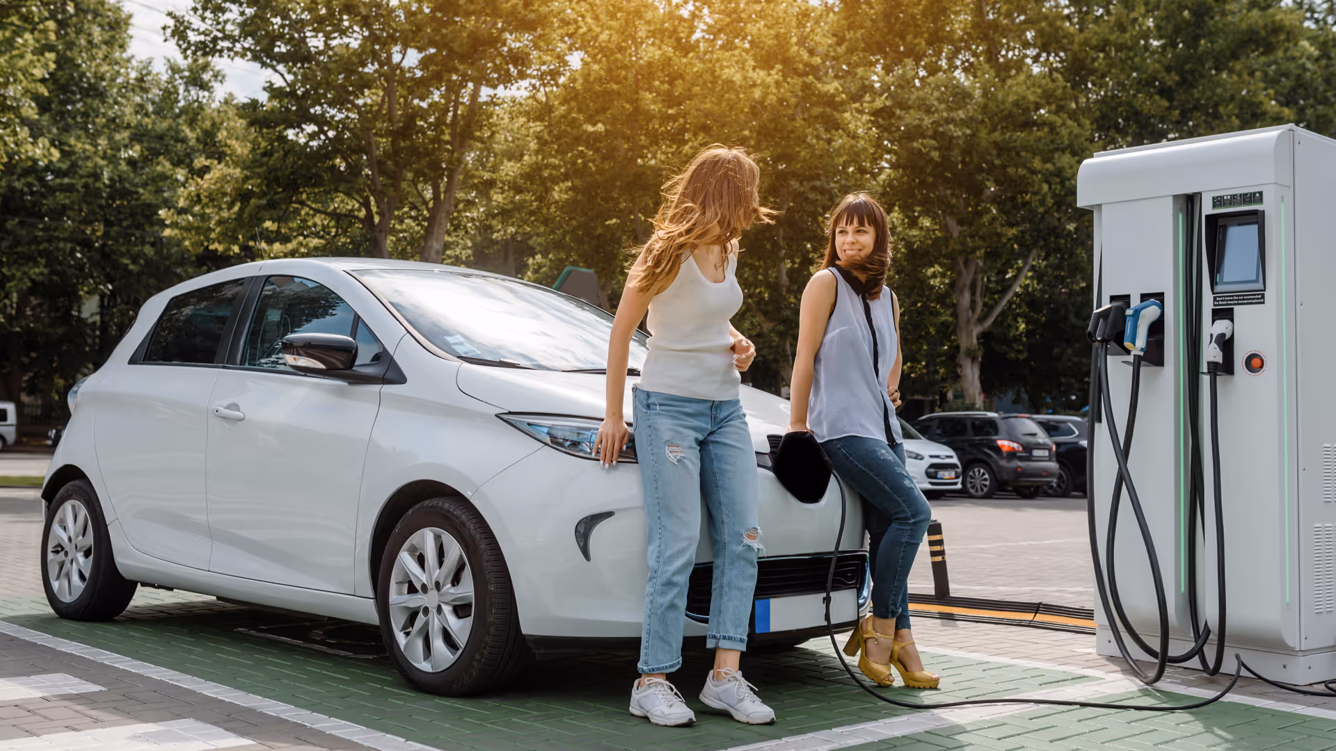 Two women next to an electric vehicle charging at a public station, highlighting sustainable transportation and everyday EV usage.